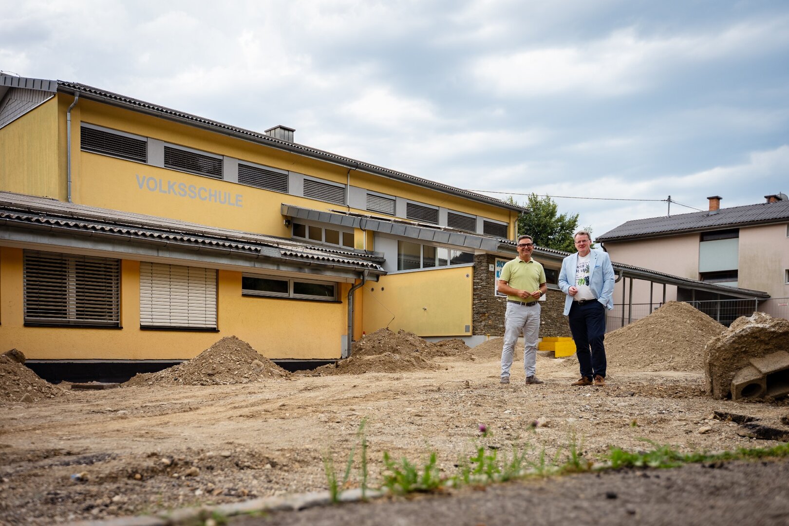Volksschule mit zwei Männern vor dem Gebäude, Baustelle in St. Johann im Pongau
